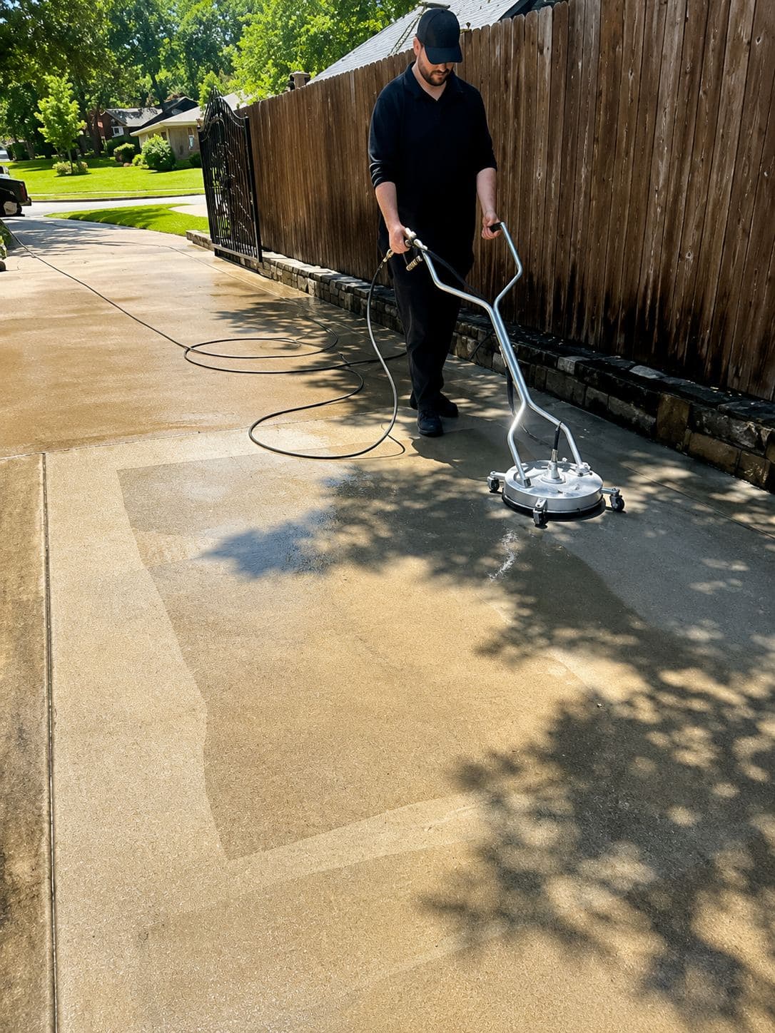 Man using a circular surface cleaner to pressure wash a dirty residential concrete driveway.